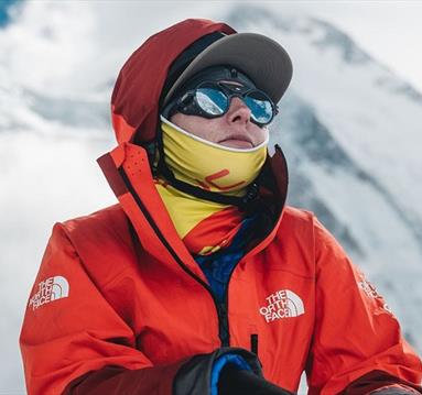 Mountaineer Adriana Brownlee pictured wearing an orange hiking jacket in front of a snow-covered mountain