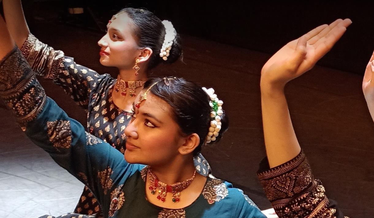 Four people dancing wearing black and gold sarees