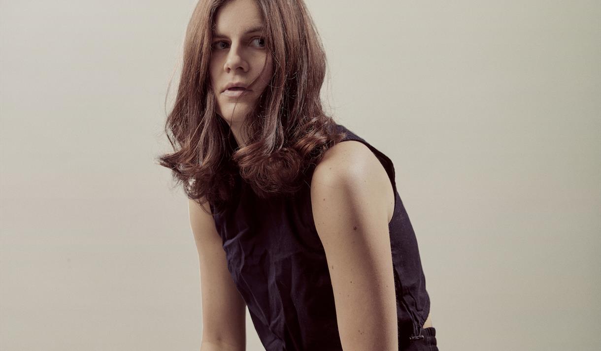 Image shows Micky Overman sat on a wooden stool looking into the camera.