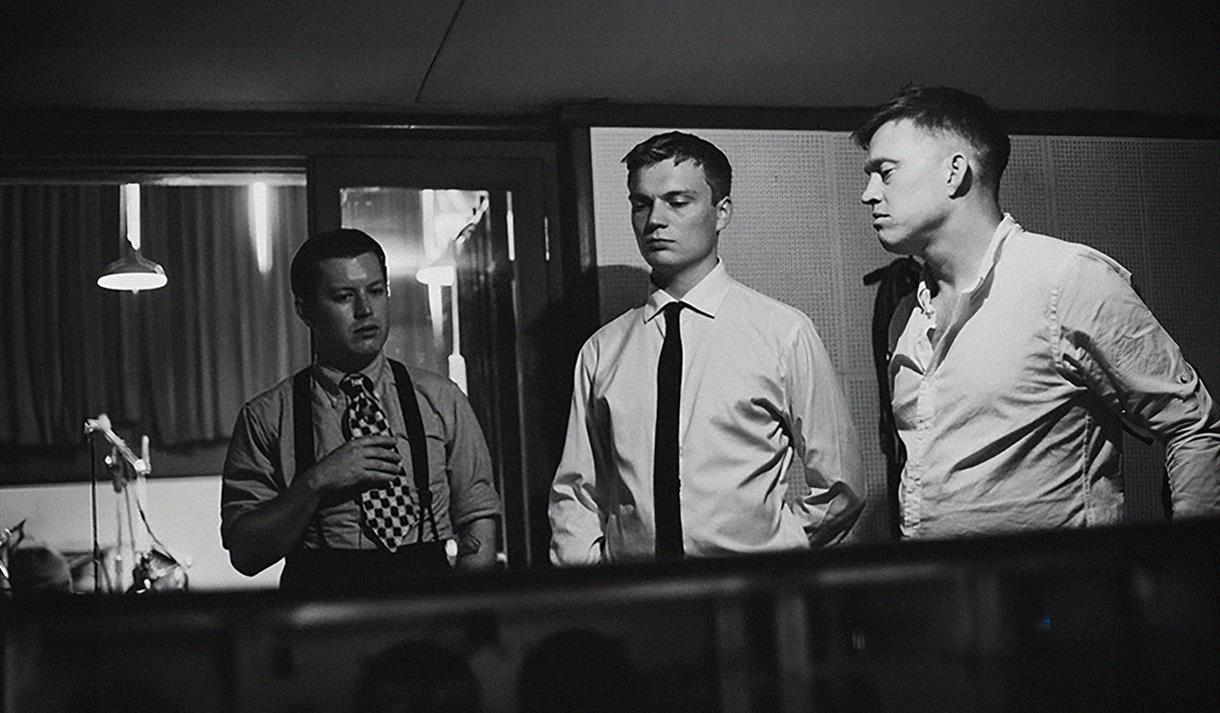 Adrian Cox, Will Sach and Alex "Honey" Boulton have a discussion in a recording studio.