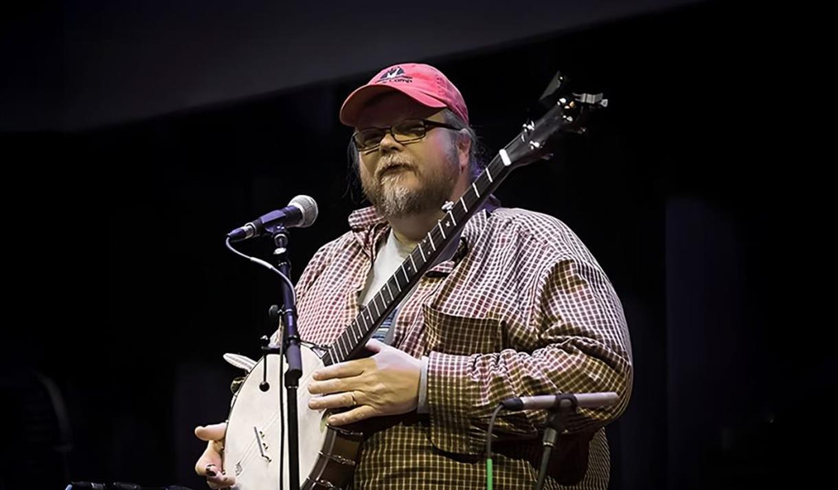 Riley Baugus speaks, banjo in hand, to the audience between numbers