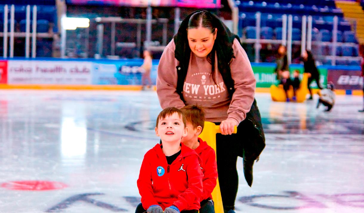 Photo of a mum and two young boys enjoying an ice-skating session, using ice equipment