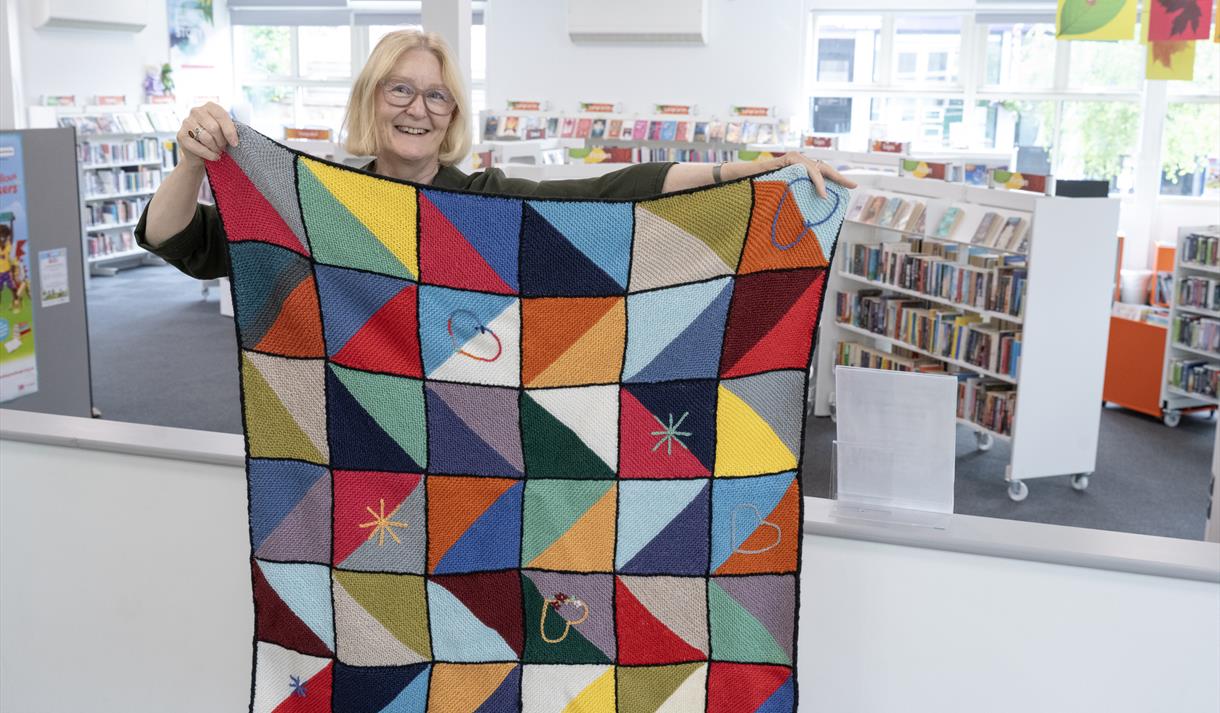 Photo of a woman holding up a blanket made from crochet squared