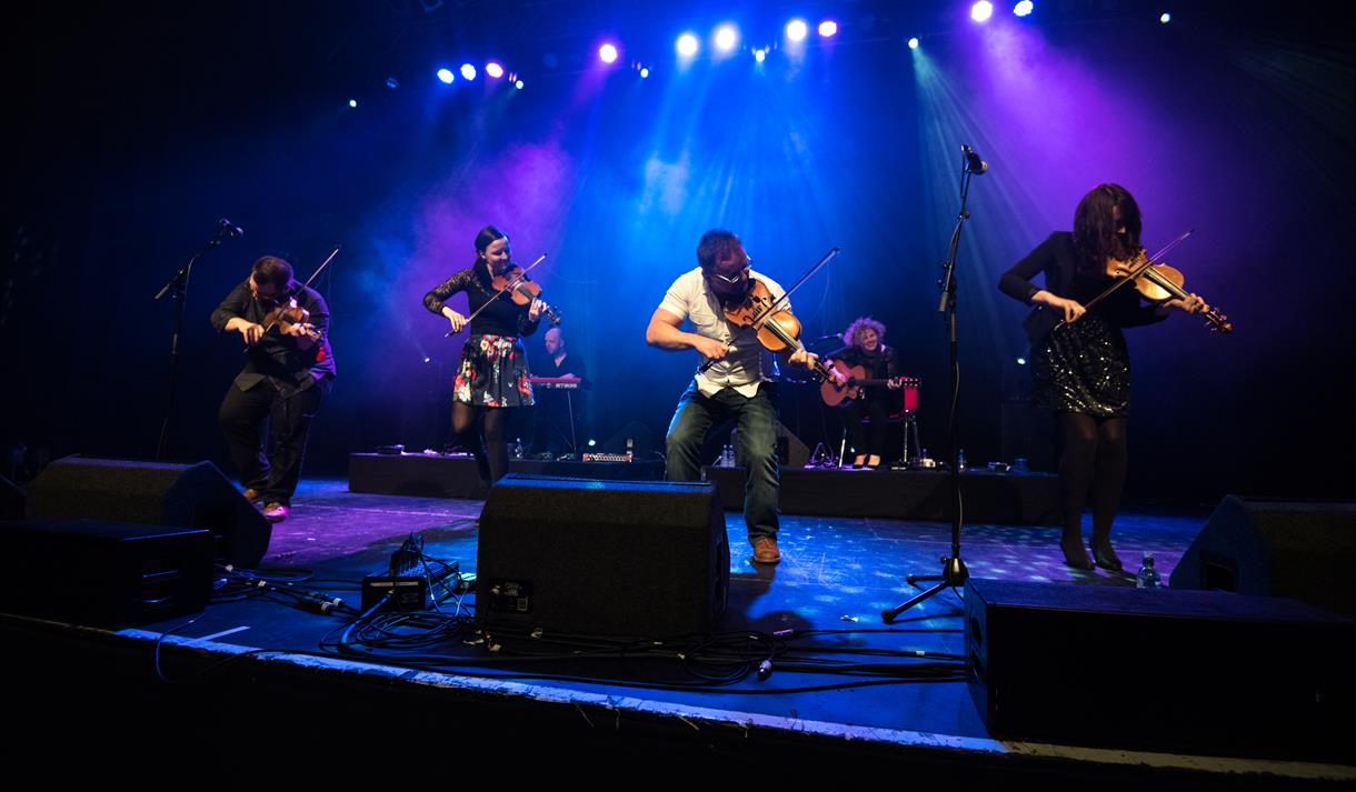 Band playing violins on a blue lit stage.