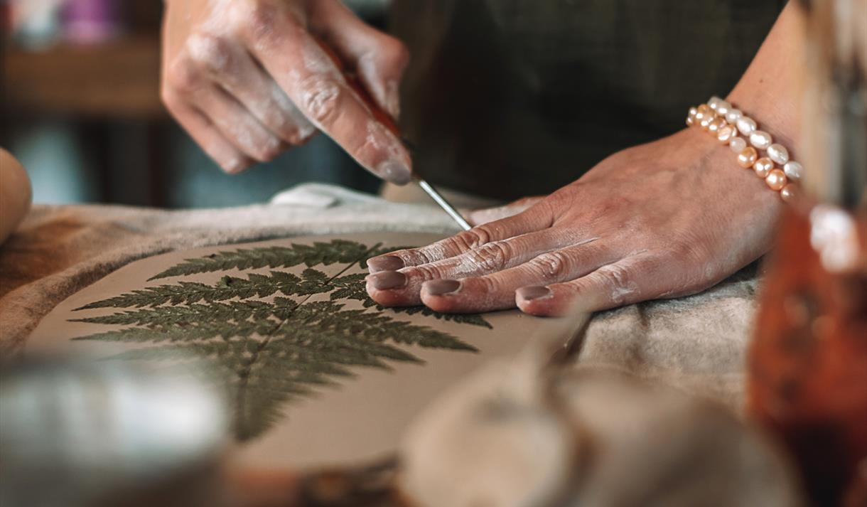 Photo of a person engaged in an activity on a tabletop. They appear to be undertaking a craft with clay and leaves,