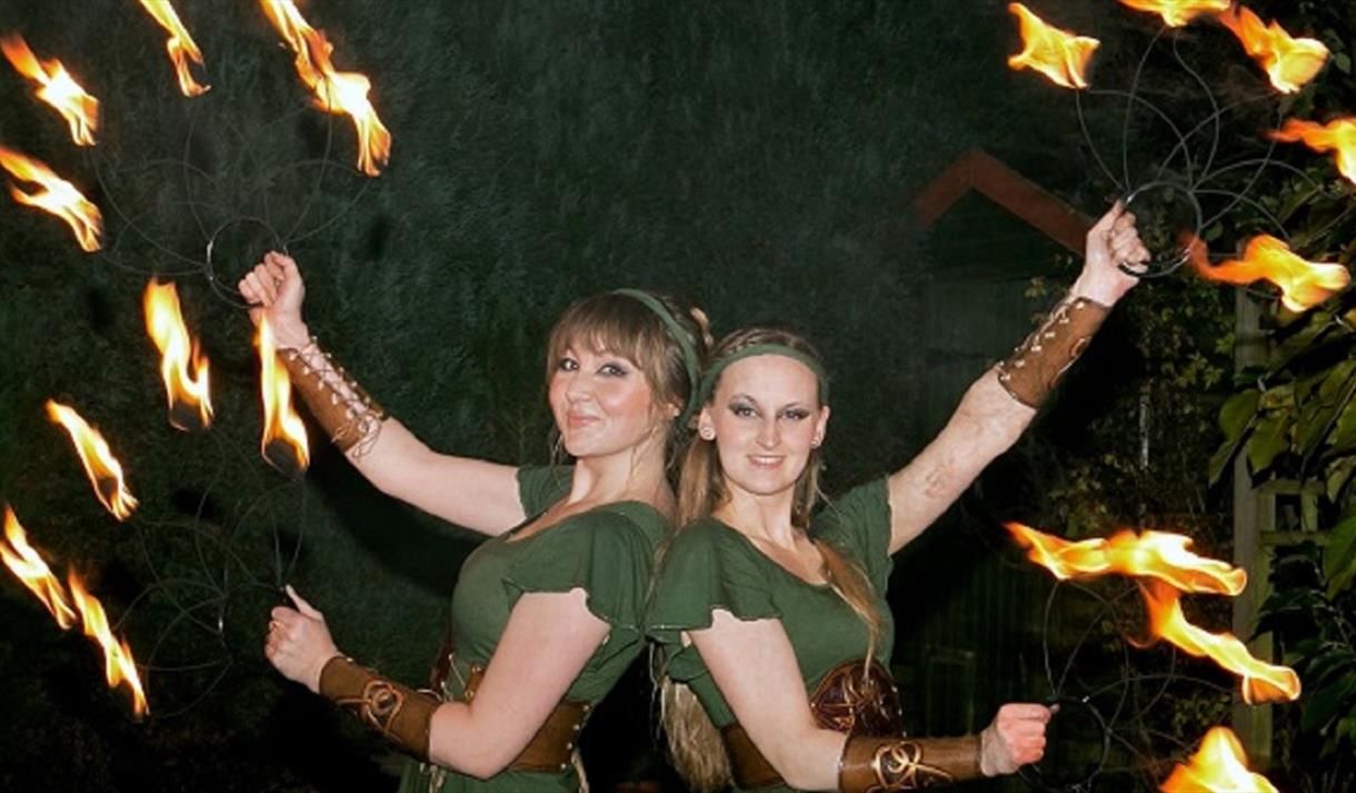 Two women in Robin Hood costumes juggling with fire