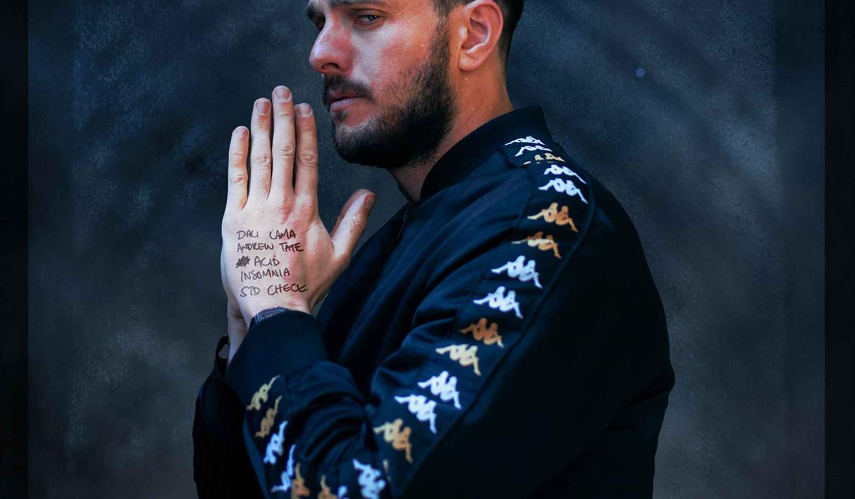 The image shows Mike Rice in a black jumper stood looking into the distance with his hands in a prayer position.