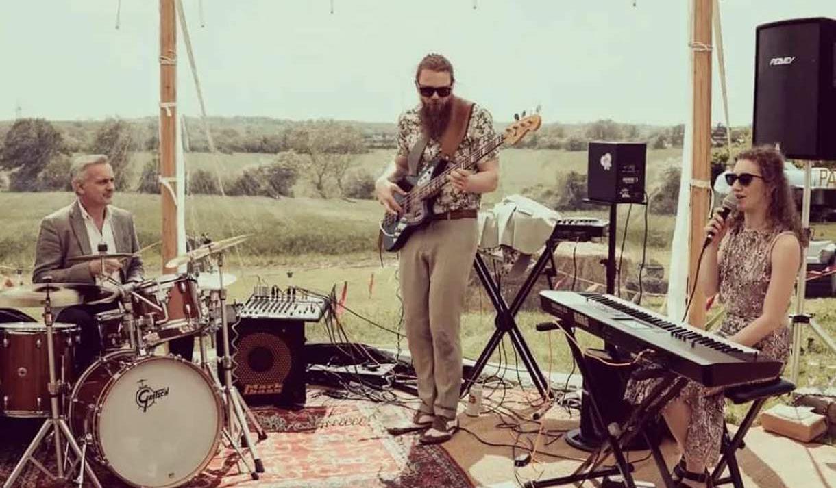 Shot of Mucky slide playing on stage in a gazebo looking out over rolling countryside