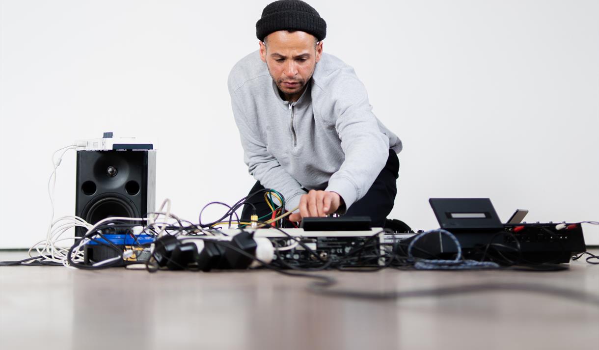 Photograph of Tom Harris sitting ont he floor with tape equipment surrounding him.