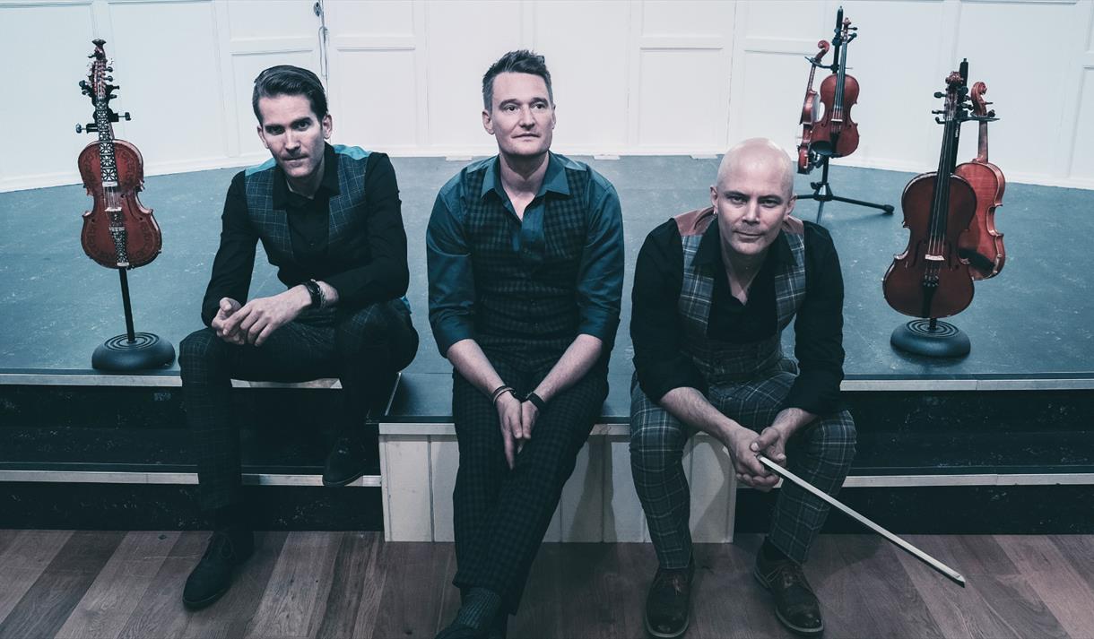 Photo of the The Nordic Fiddlers Bloc casully sitting ont he edge of a stage.