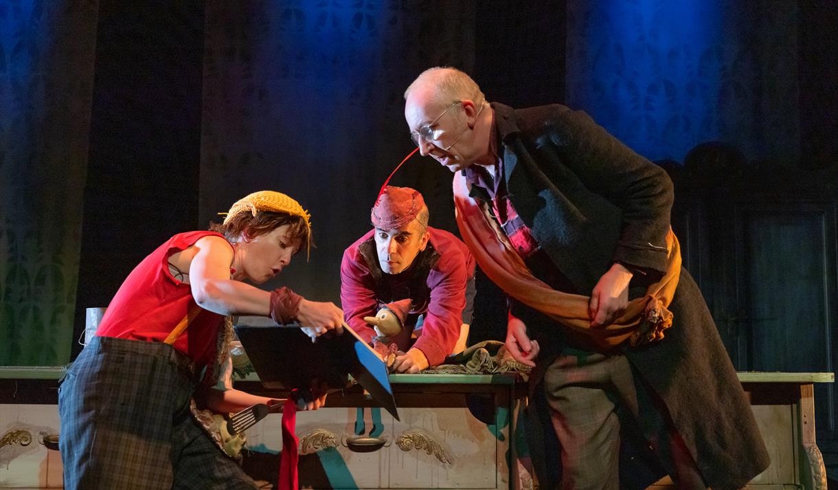 Image shows three people on stage looking at a storybook together.