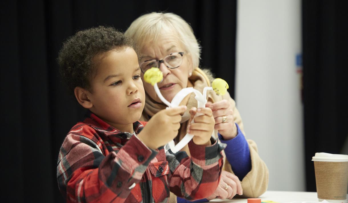 Image shows a child and an older lady looking at a headband which they've made.