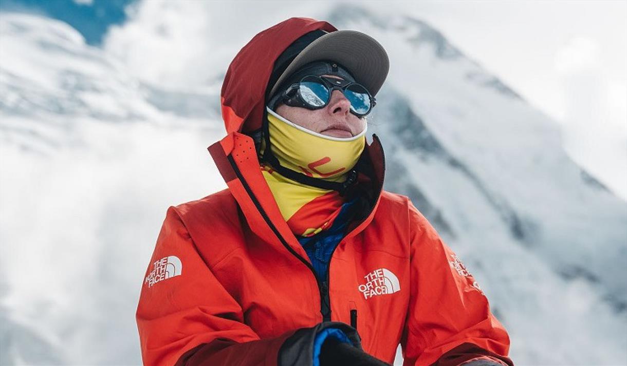 Mountaineer Adriana Brownlee pictured wearing an orange hiking jacket in front of a snow-covered mountain