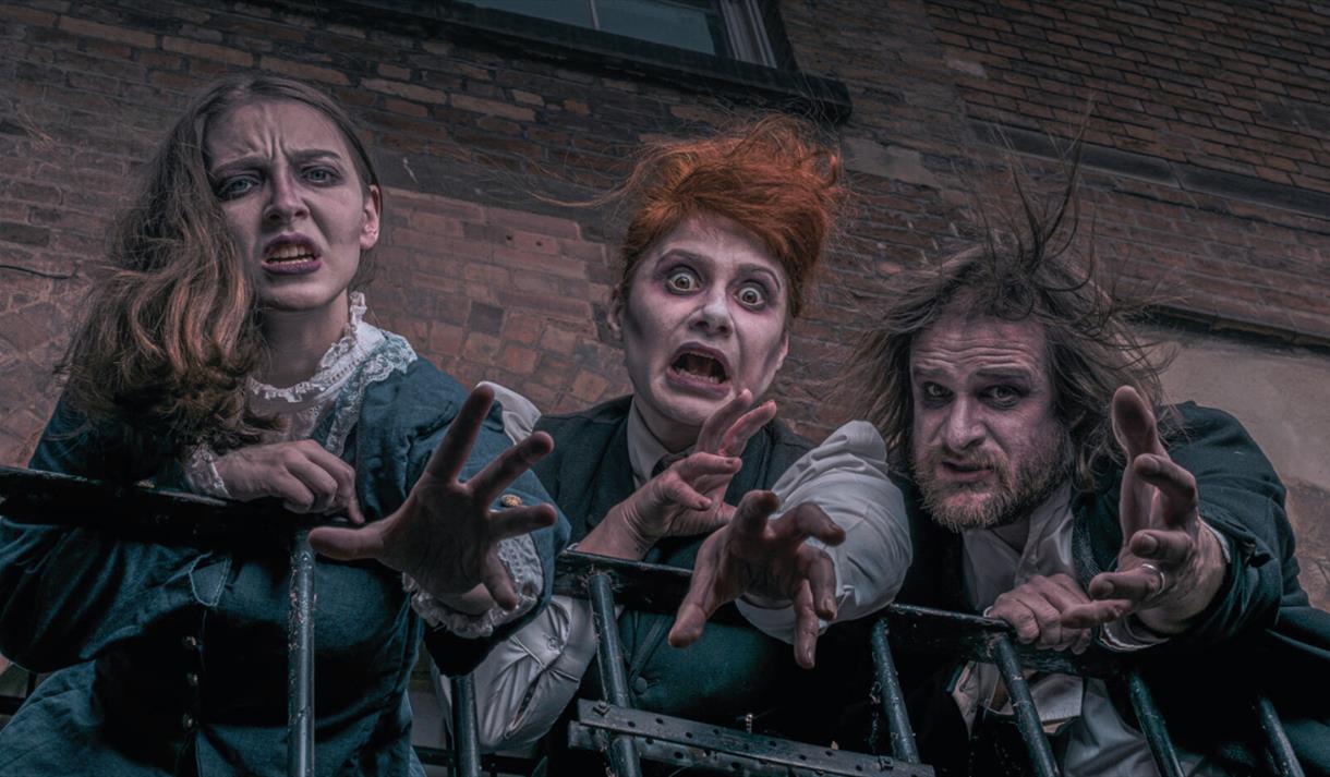 Three characters dressed as Victorian ghosts beckoning the camera