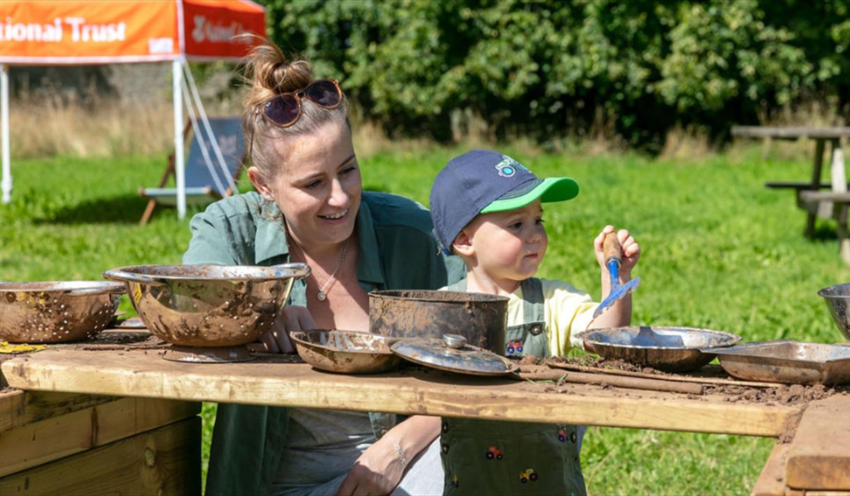 Photo of a woman and a chil in the sunshine. They seem to be engaging in an acitvity involving pots and pans.