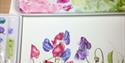 paintings of pink and purple flowers next to a paint palette of the same colours