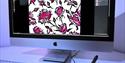 a desktop computer showing a pink and black floral design, with a hand holding a pen to a digital drawing pad